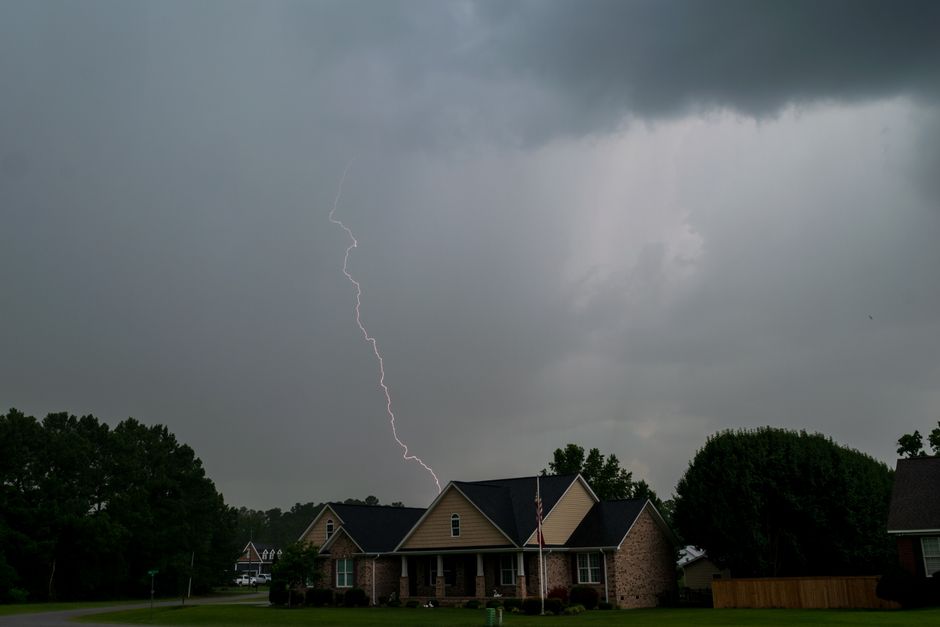 A vivid lightning bolt pierces the sky over suburban houses during a storm, capturing nature's raw power.